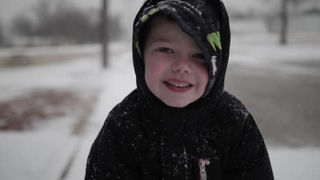 Young,-happy-boy-smiling-and-wearing-a-coat-playing-outside-on-a-cold,-winter-day-in-December-in-the-snow-during-Christmas-break-in-a-small-town-in-the-midwest