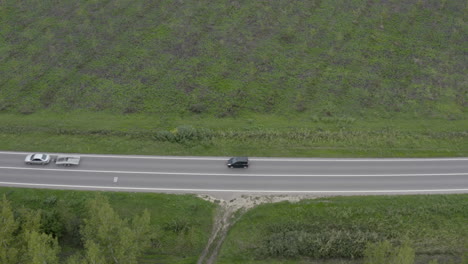Aerial-shot-of-two-cars-driving-along-the-road-through-wooded-landscape,-drone-pov