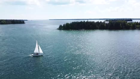 Aerial-of-Sailboat-and-forested-islands-in-summer-sun---Hessel,-Michigan---Lake-Huron
