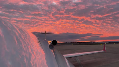 Extraordinary-red-sky-reflected-on-the-upper-fuselage-of-a-jet-just-before-sunset,-unfocused-focused-view,-with-a-follow-me-car-at-the-back