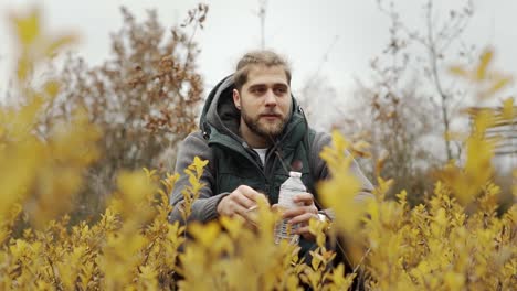 Man-smoking-in-a-field-with-yellow-flowers-while-holding-a-water-bottle