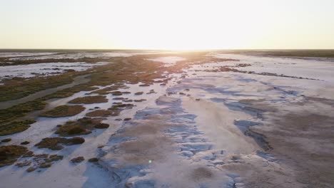 moving-aerial-view-of-a-salt-field,-with-little-vegetation-and-a-sunset-sky