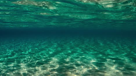 Authentic-under-water-scene-of-crystalline-turquoise-tropical-ocean-water-with-rippled-surface-and-reflections-on-seafloor-with-blue-background