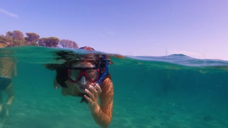 Half-underwater-scene-of-little-girl-with-diving-mask-and-snorkel-swimming-in-turquoise-tropical-sea-water-of-exotic-island