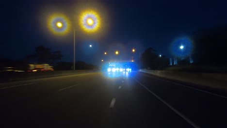 Rear-facing-night-driving-point-of-view-POV-for-interior-car-scene-green-screen-replacement---driving-along-a-busy-suburban-freeway-or-motorway,-exiting-down-a-dark-slip-lane
