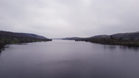 Drone-shot-flying-forward-over-a-lake-on-a-dark-and-moody-day,-wide,-aerial