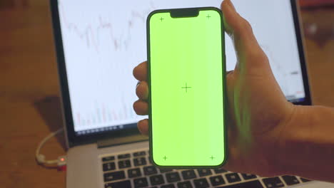 Iphone-13-Pro-with-Chroma-Key-Background-with-Financial-Chart-on-Laptop-Screen-in-the-Background