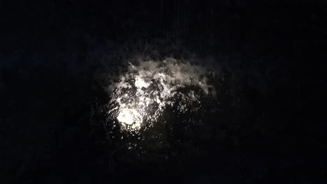 Rain-droplets-on-puddle-,-dark-night