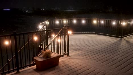 Fresh-gently-snow-falling-on-a-peaceful-night---static-view-of-a-lit-patio-or-deck