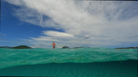 Half-underwater-pov-of-man-having-fun-practicing-sup-on-surf-board-or-standup-paddleboard-over-sea-water-surface