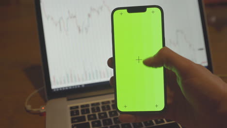 Scrolling-on-Iphone-13-Pro-with-Chroma-Key-Background-with-Financial-Chart-on-Laptop-Screen-in-the-Background