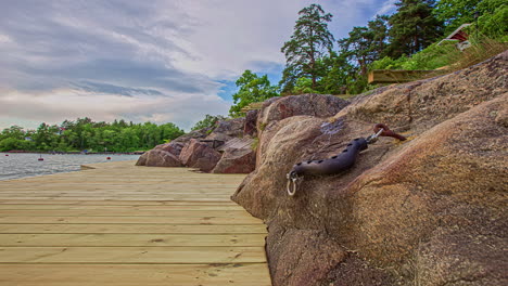 Shot-of-a-wooden-pier-along-rocky-slope-beside-a-calm-lake-on-a-cloudy-evening-in-timelapse