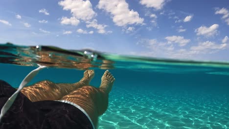 First-person-view-of-male-legs-and-feet-floating-on-beautiful-clear-and-transparent-ocean-water-of-exotic-island