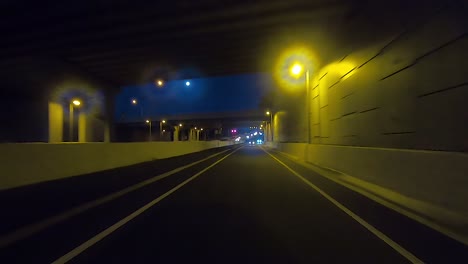 Rear-facing-night-driving-point-of-view-POV-for-interior-car-scene-green-screen-replacement---driving-through-yellow-lit-underpasses-and-bridges-through-a-major-freeway-intersection