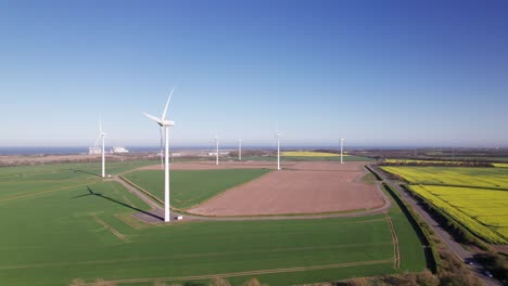 Panning-drone-shot-of-wind-turbines-on-a-summer-day,-wide,-aerial