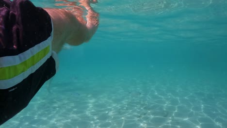 Underwater-personal-perspective-view-of-man-legs-floating-in-clear-transparent-sea-water-with-beneath-surface,-slow-motion