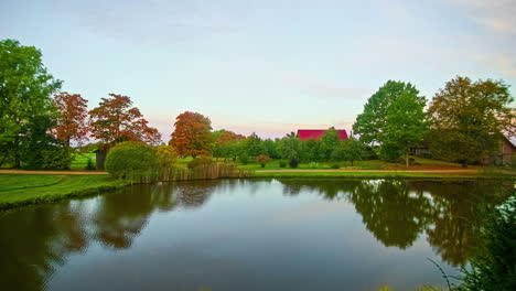 Lake-in-bucolic-and-idyllic-green-landscape-with-red-roof-in-background