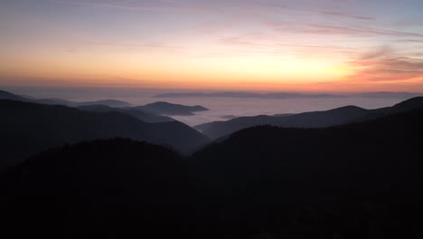 Aerial-cinematic-scene-with-a-sunset-above-the-mountains-covered-in-fog