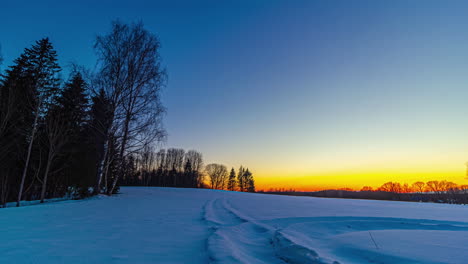 Sun-setting-down-with-vibrant-bright-colors-behind-snowy-rural-landscape,-fusion-time-lapse