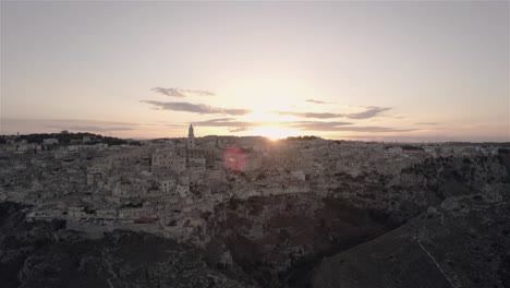 Drone-flying-upwards-and-forwards-towards-the-old-city-of-Matera-at-sunset-in-south-Italy-in-4k