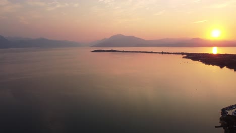Aerial-shot-of-Lake-Garda-at-sunrise-with-Sirmione-and-mountains-in-the-back