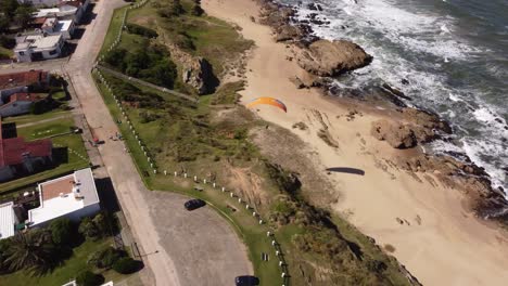 Aerial-shot-of-Paraglider-flying-over-rocky-beach-in-a-sunny-day-4K