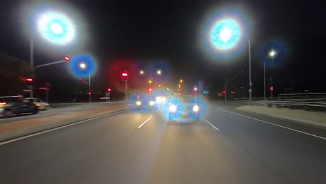 Rear-facing-night-driving-point-of-view-POV-for-interior-car-scene-green-screen-replacement---rush-hour-evening-traffic-on-a-suburban-dual-lane-road-and-exiting-into-dark-street