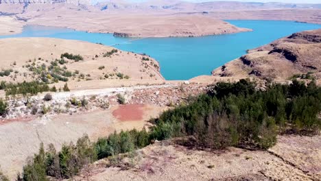 Aerial-shot-ascending-above-the-tree-line-to-reveal-a-scenic-view-of-the-Driekloof-Dam,-its-blue-waters-adding-colour-to-the-dry-arid-winter-landscape-surrounding-the-dam,-Free-State,-South-Africa