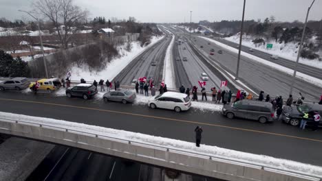 Cinematic-fly-over-of-Canadian-Protestors-Waving-Flags-Standing-on-Highway-Bridge-in-Support-of-Freedom-as-Trucks-drive-past