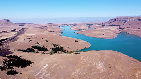 Aerial-drone-shot-of-the-scenic-mountainous-landscape-and-dry-savannah-grasslands-which-surround-the-beautiful-blue-waters-of-the-Driekloof-Dam,-Free-State,-South-Africa