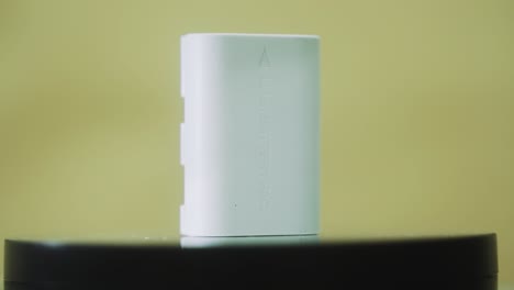 A-rotating-close-up-shot-of-a-standing-white-lithium-camera-battery,-slow-motion-4K