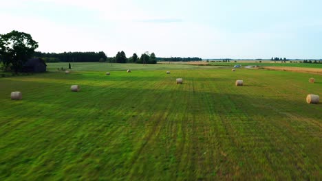 Fly-Fast-Over-Greenery-Landscape-With-Scattered-Hay-Bales-At-The-Farmland