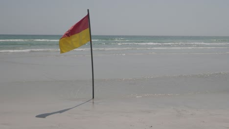 Static-shot-of-yellow-red-safety-flag-on-a-windy-day-on-the-ocean-beach-waving-in-the-wind-due-to-the-strong-currents-in-the-water