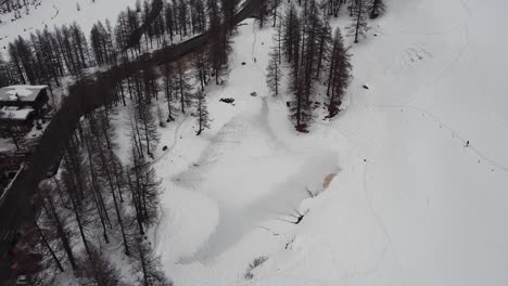 Aerial-view-of-a-frozen-lake-in-a-mountain-valley-in-Valle-D'Aosta,-in-the-Italian-Alps,-in-winter