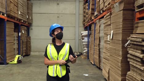 A-female-employee,-walking-through-the-storage-area-of-a-warehouse,-inspecting-the-shelves-and-tapping-on-a-touchpad