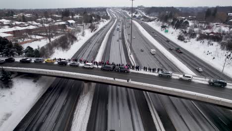 Canadian-Protestors-Wave-Flags-on-Windy-Day,-Standing-on-the-edge-of-busy-highway-overpass