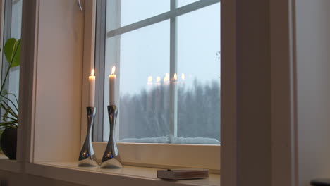 Beleuchtete-Kerzen-Auf-Der-Fensterbank,-Die-Auf-Fenster-Mit-Schnee-Reflektieren
