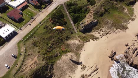 Holidaymaker-enjoying-paragliding-from-beachside-cliffs-at-La-Pedrera-village-on-Atlantic-Coast,-Uruguay