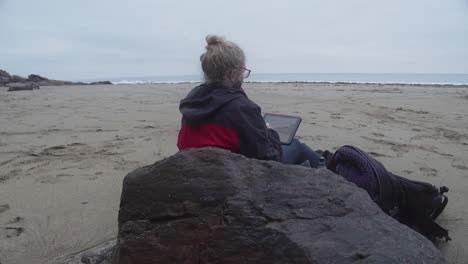 Eine-Frau-Sitzt-Auf-Einem-Felsen-Zeichnet-Auf-Einem-Tablet-Den-Wunderschönen-Meerblick-In-Spülkopf-Und-Bucht,-Cornwall,-England,-Vereinigtes-Königreich