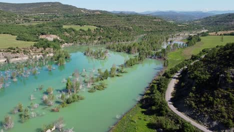 Congost-de-Mont-Rebei-Canyon-at-Ager,-Catalonia-and-Aragon,-Spain---Aerial-Drone-View-of-the-Blue-Emerald-Noguera-Ribagorzana-River-with-Trees-Under-Water-and-Green-Valley