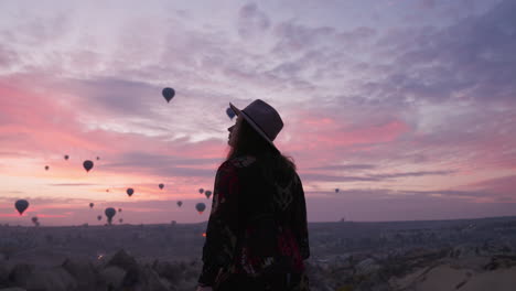 Schöne-Weibliche-Touristin-In-Kleid-Und-Hut,-Die-Heißluftballons-Beobachten,-Die-Bei-Sonnenaufgang-über-Kappadokien-In-Der-Türkei-In-Den-Himmel-Fliegen