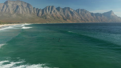 Surfistas-En-La-Playa-De-La-Bahía-De-Kogel-Con-Vistas-A-Las-Montañas-De-Kogelberg-En-Ciudad-Del-Cabo,-Sudáfrica