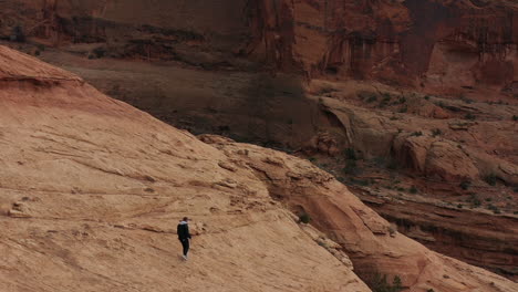 Luftbild-Eines-Mannes,-Der-Auf-Einem-Hügel-Von-Sandsteinhügeln-In-Der-Wüste-Von-Utah-Läuft-Und-Einen-Drohnenschuss-Verfolgt