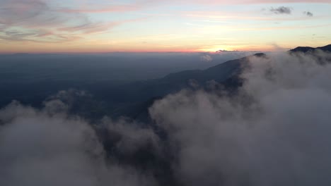 Moody-sunset-above-dark-silhouette-mountain-range-above-clouds,-aerial