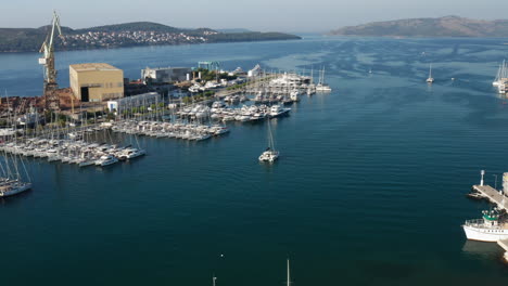 Aerial-View-Of-Catamaran-Boat-Sailing-In-The-Sea-Passing-By-Marina-And-Shipyard-In-Trogir,-Croatia
