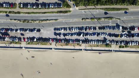 Sandiger-Ozeanstrand-Parkplatz-Von-Oben-Nach-Unten-Mit-Autos,-Die-Auf-Die-Straße-Fahren