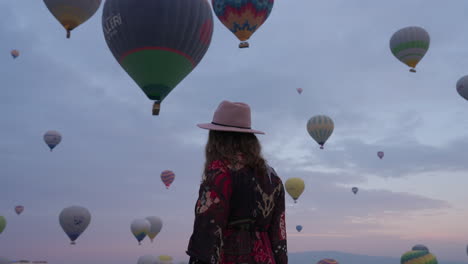 Woman-Walking-And-Admiring-Beautiful-And-Majestic-View-Of-Cappadocia-With-Numerous-Air-Balloons-In-Flight---medium-shot
