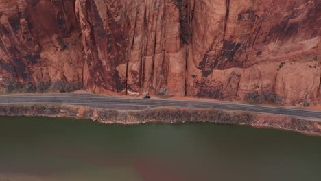 Aerial-View,-Dark-Vehicle-Parked-by-the-Road-by-Colorado-River-and-Steep-Cliffs-of-Utah-Desert,-Tilt-Down-Drone-Shot