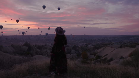 Girl-Running-Towards-A-Cliffside-to-Get-A-Better-View-Of-Hot-Air-Balloons-In-Flight-In-Cappadocia-Turkey---panning-shot