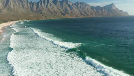 Luftaufnahme-Von-Surfern-Und-Schäumendem-Ozean-Am-Strand-Von-Kogel-Bay,-Kapstadt,-Südafrika---Drohnenaufnahme